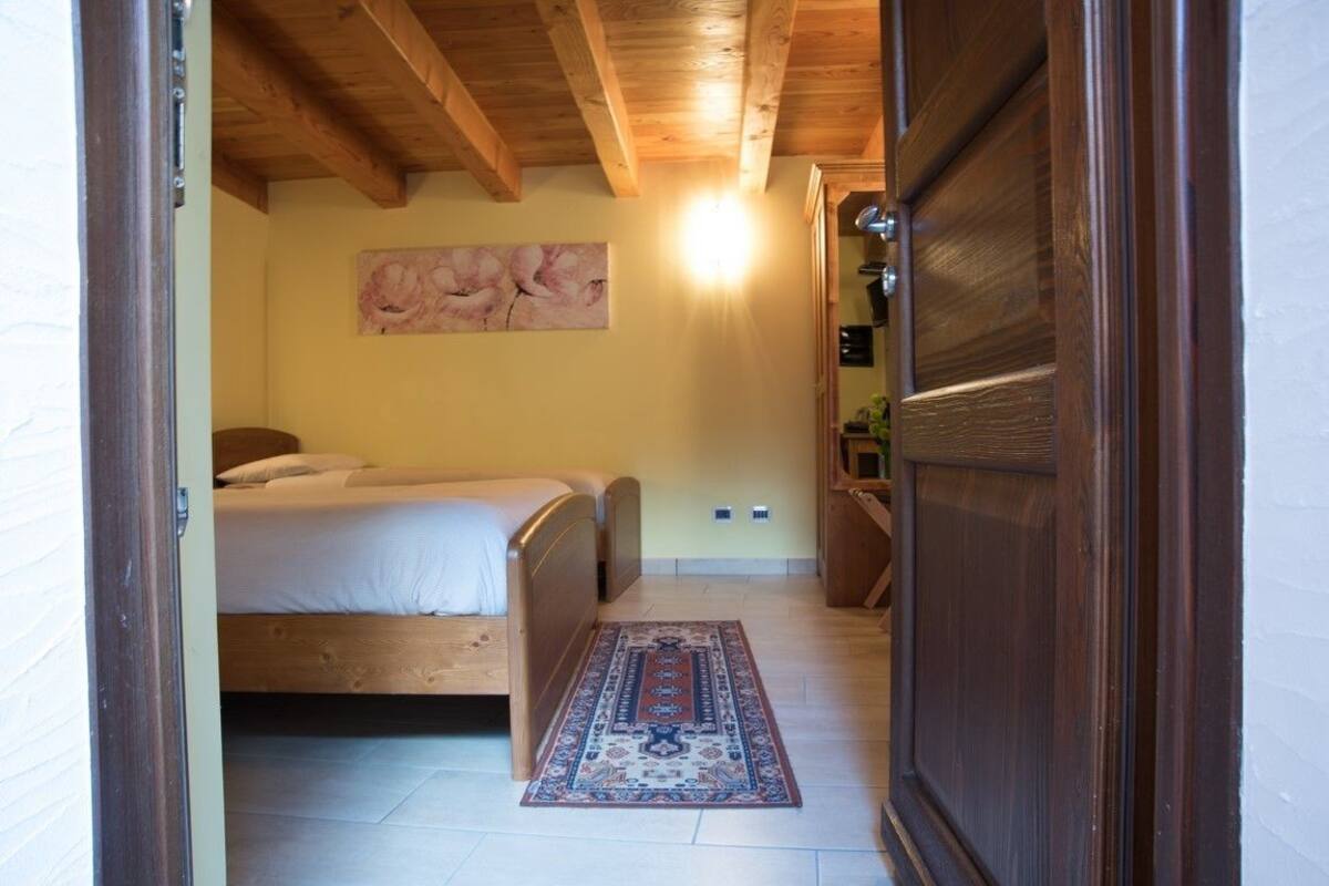 A bedroom with a wooden ceiling, a bed, a rug, and a painting on the wall.