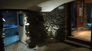 Habitación con paredes y suelo de piedra, una ventana y vista a una piscina al aire libre.