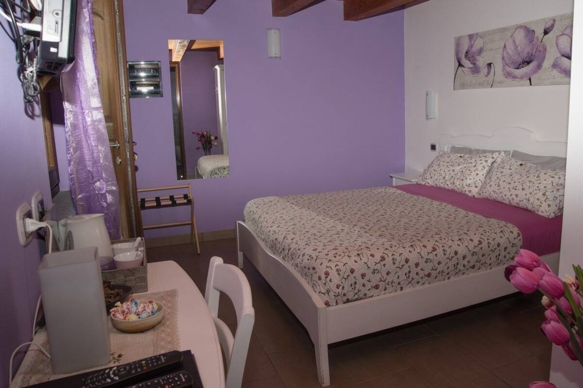 A bedroom with a bed, a desk with a computer, a chair, a mirror, and a painting on the wall.