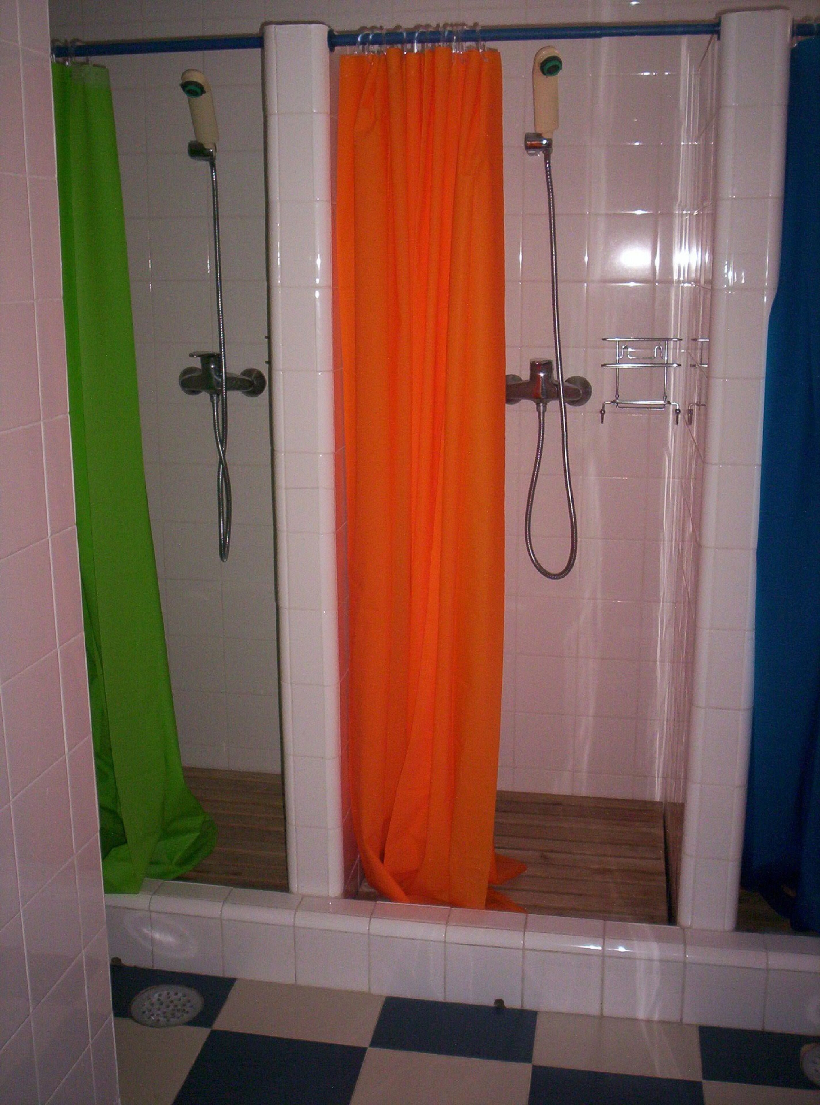 Un baño con piso a cuadros, cortina de ducha verde, cortina de ducha naranja y cortina de ducha azul.