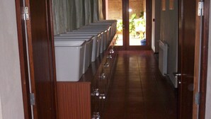 Un couloir bordé d’une rangée de réfrigérateurs blancs sur le côté gauche, avec un sol carrelé et des portes en bois de chaque côté.