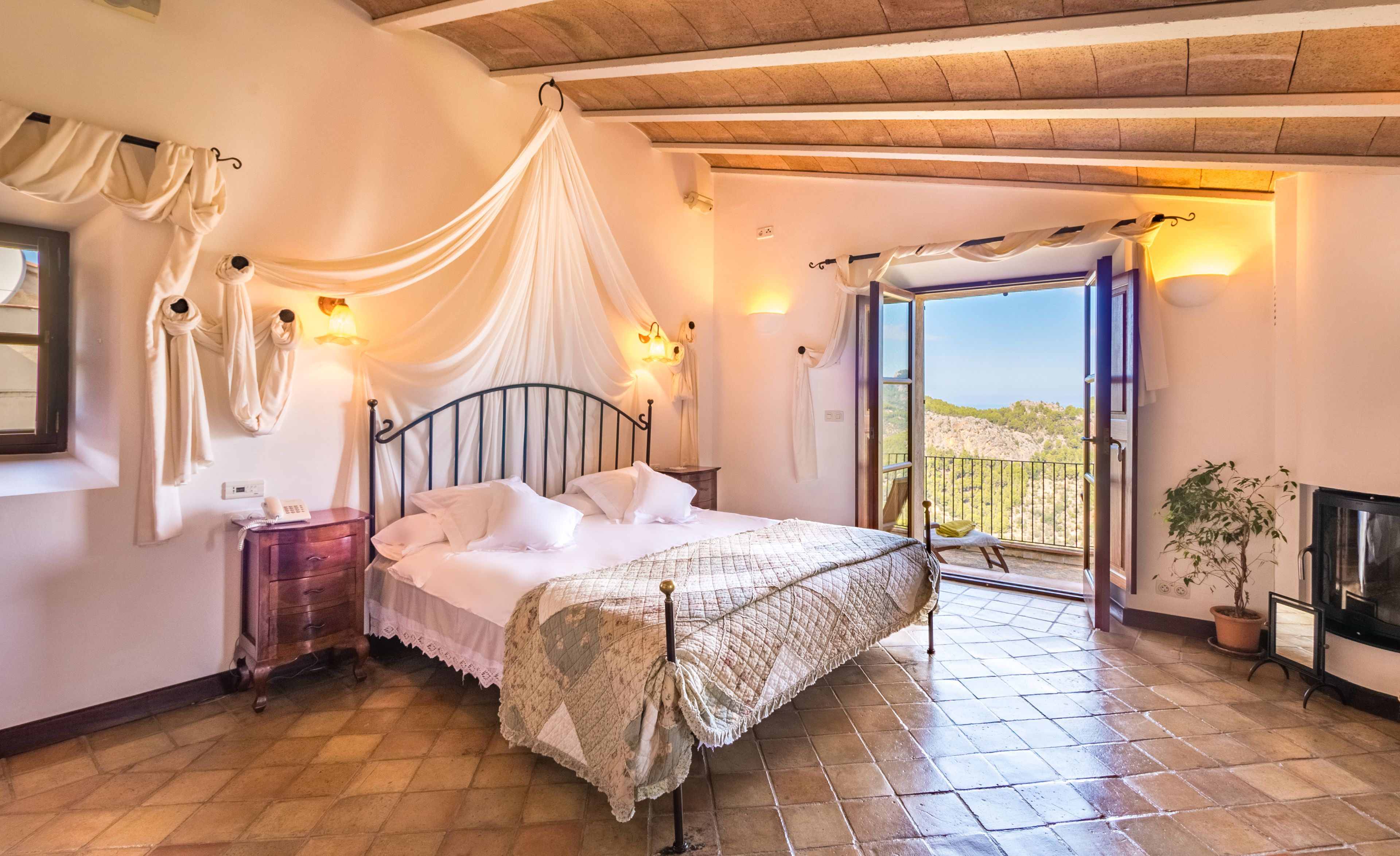 Ein Schlafzimmer mit Bett, Nachttisch, Fenster und Blick ins Freie.