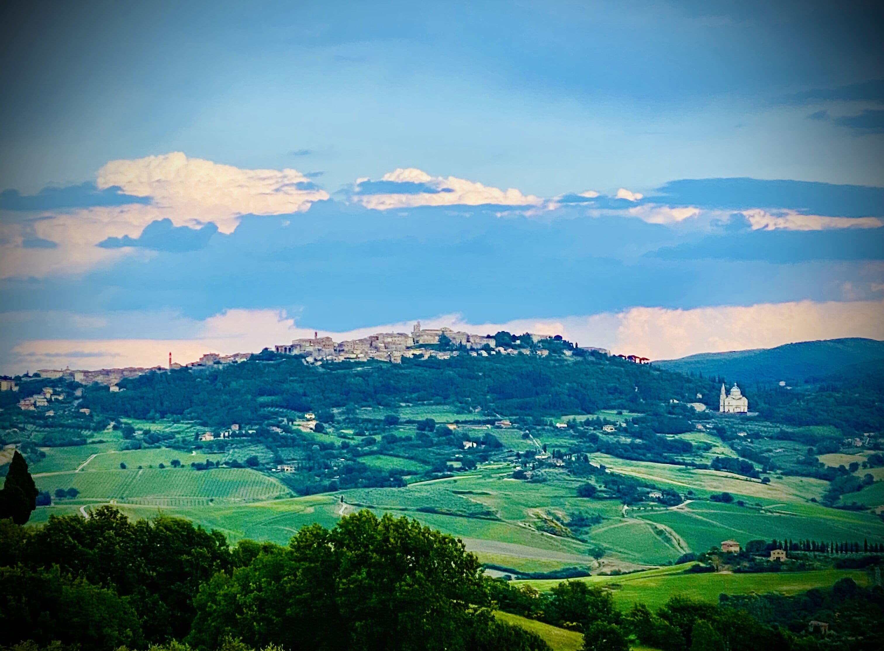 A panoramic view of a hilly landscape with a prominent castle on a hill, surrounded by green fields and a few scattered buildings.