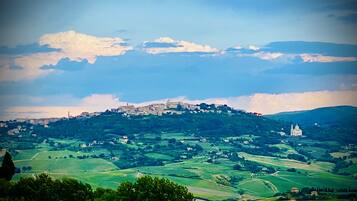 A panoramic view of a hilly landscape with a prominent castle on a hill, surrounded by green fields and a few scattered buildings.