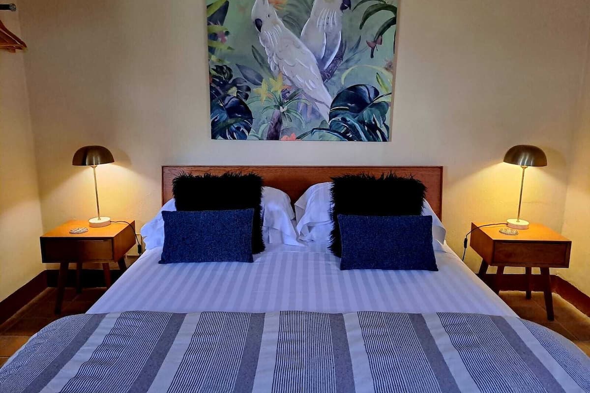 A hotel room with a large bed, two nightstands, two lamps, and a painting of birds on the wall.