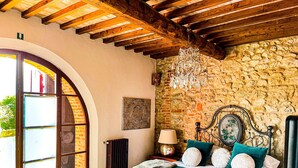 A bedroom with a stone wall, a bed with teal bedding, a chandelier, and a view through a glass door. - LaChiusa Tuscany (Torrita di Siena)