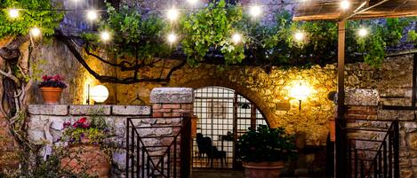 An outdoor patio area with a stone wall, a wooden pergola, and string lights.