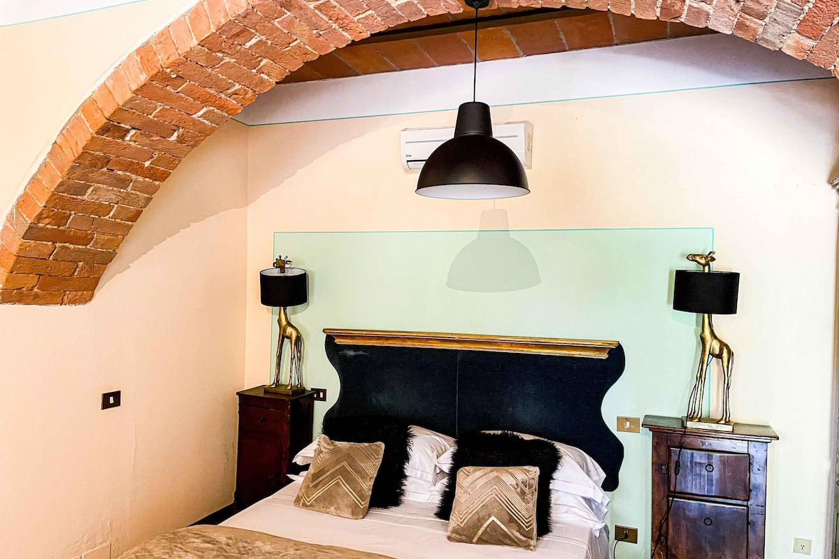 A bedroom with a brick arch, a bed with two nightstands, a hanging lamp, and a wooden cabinet.