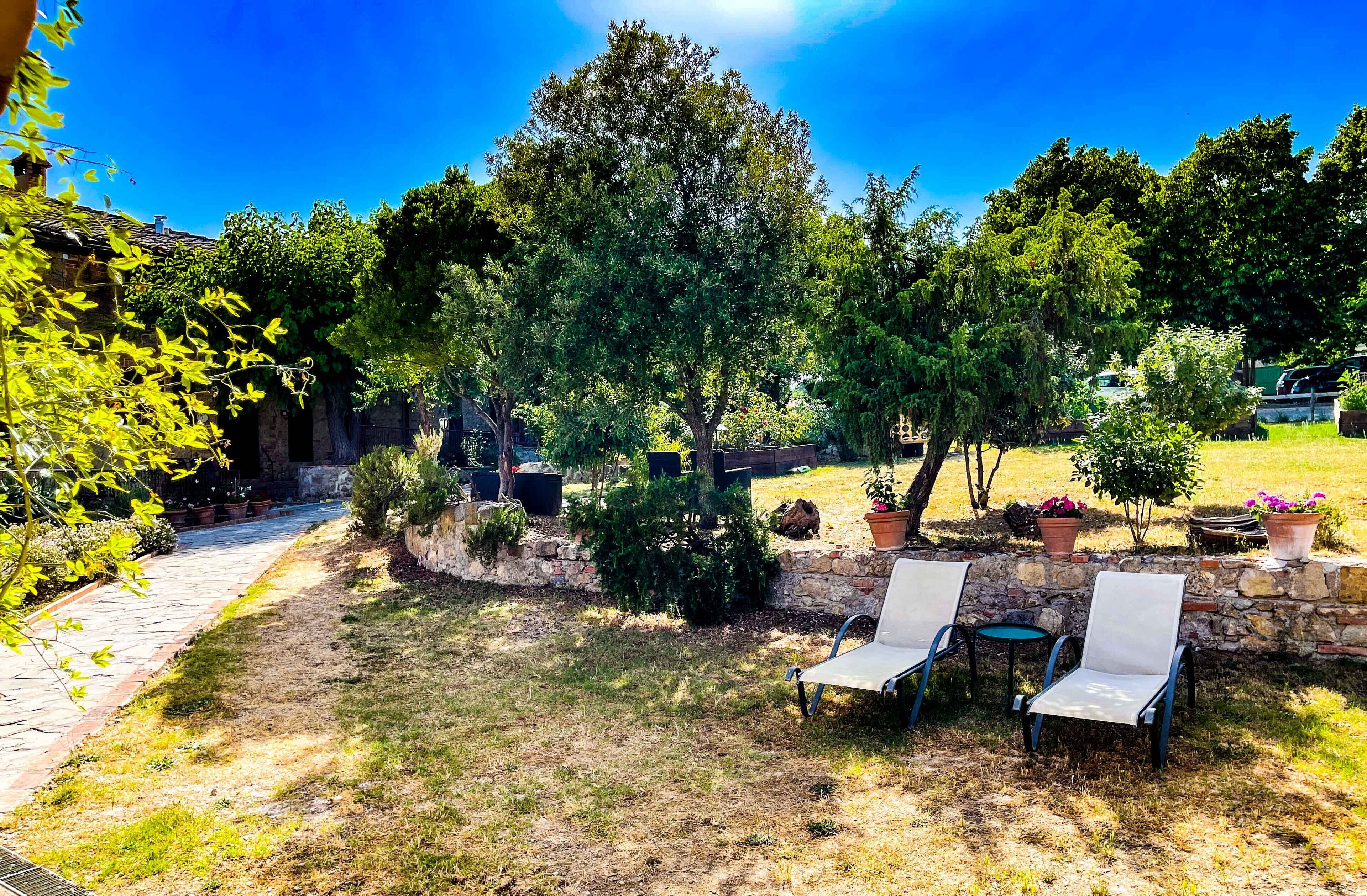 Un jardín con muros de piedra, plantas en macetas y dos sillones blancos.