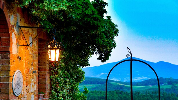 A rustic brick wall with a lantern and a metal archway overlooking a lush valley. - LaChiusa Tuscany (Torrita di Siena)