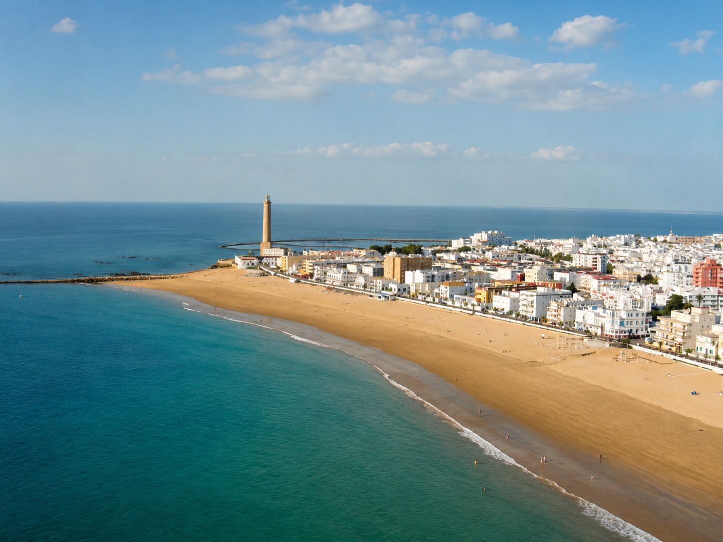 A coastal town with a lighthouse, sandy beach, and buildings along the shore.