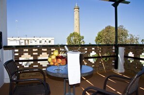 Enjoy a serene view from this balcony with a round table, wicker chair, and armchair, perfect for relaxing with a bowl of fresh fruit.