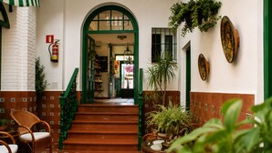 Una escalera conduce a un piso superior, flanqueada por sillas de mimbre y plantas en macetas.