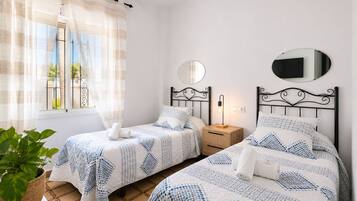 Un dormitorio con dos camas, una mesita de noche con lámpara, un espejo y una planta en maceta.