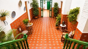 Un patio con suelo de baldosas, una verja verde, plantas en macetas y una escalera con barandales verdes.
