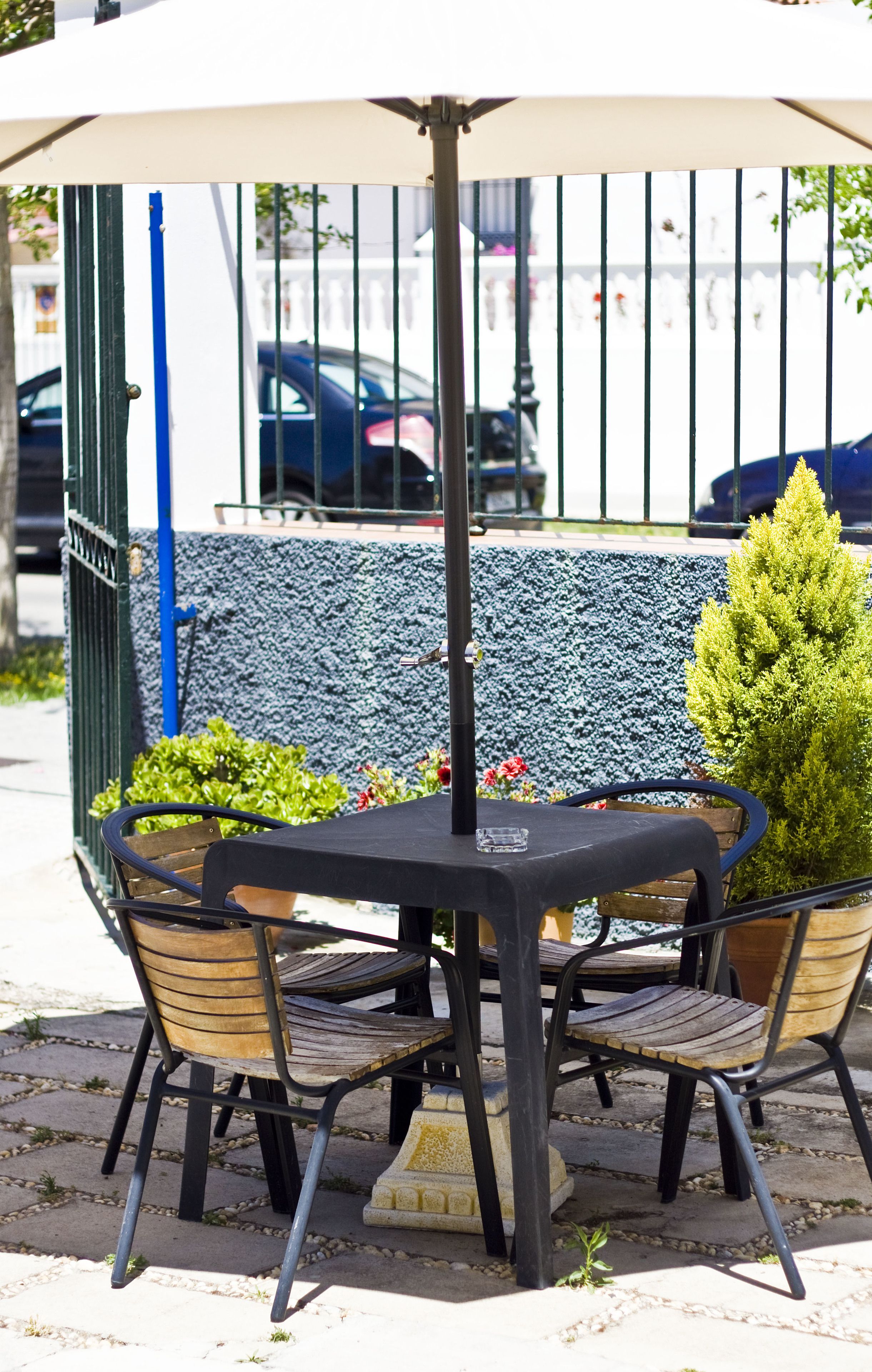 A round outdoor table with four chairs, an umbrella, and a stone planter with greenery.