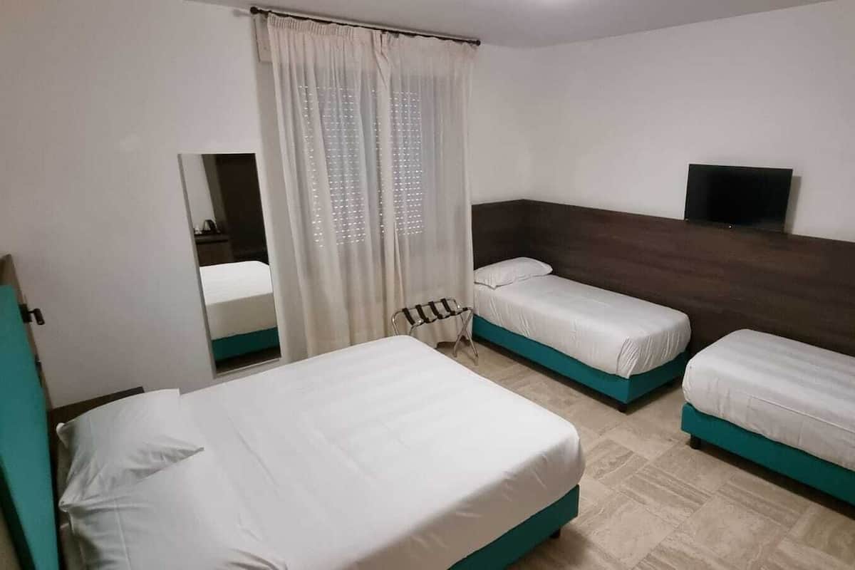 A hotel room with two single beds, a wooden headboard, a small TV, and a window with curtains.
