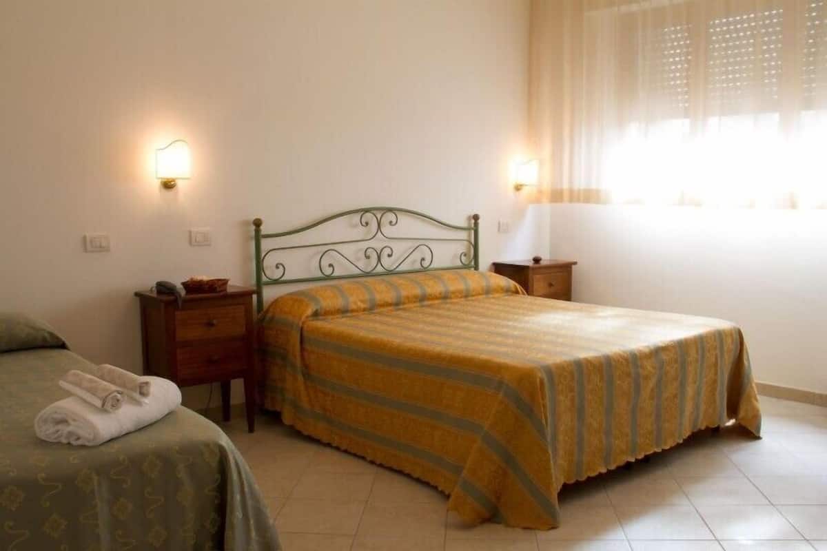 A bedroom with a bed, two bedside tables, a lamp, and a window with curtains.