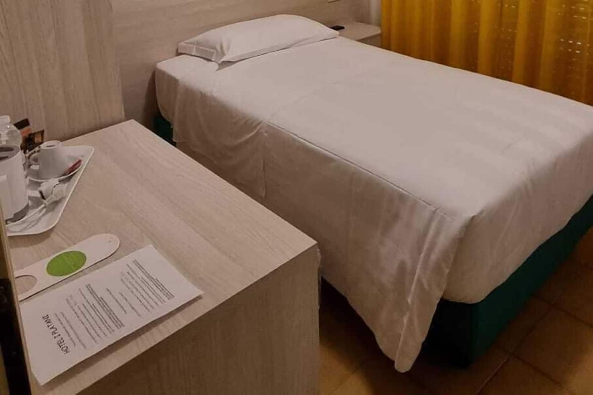 A hotel room with two single beds, a wooden headboard, a small desk with a tray of breakfast items, and a wall-mounted picture.