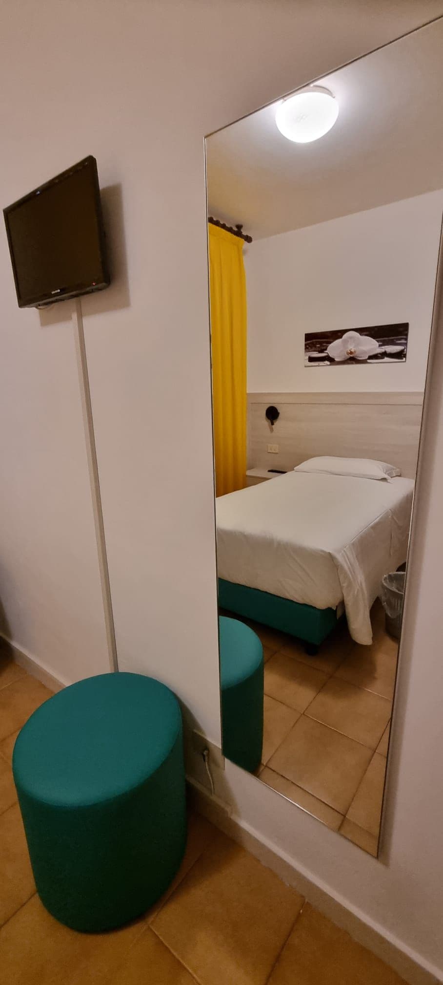 Una camera d'albergo con un letto, uno specchio, una televisione e un poggiapiedi verde.