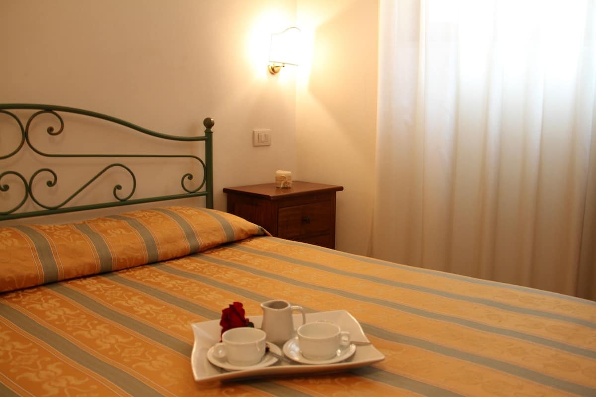 A neatly made bed with a striped bedspread, a bedside table with a lamp, and a tray with cups and a rose.