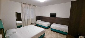 Una camera d'albergo con due letti singoli, un grande specchio, una TV a schermo piatto montata a parete e una finestra con tende bianche.