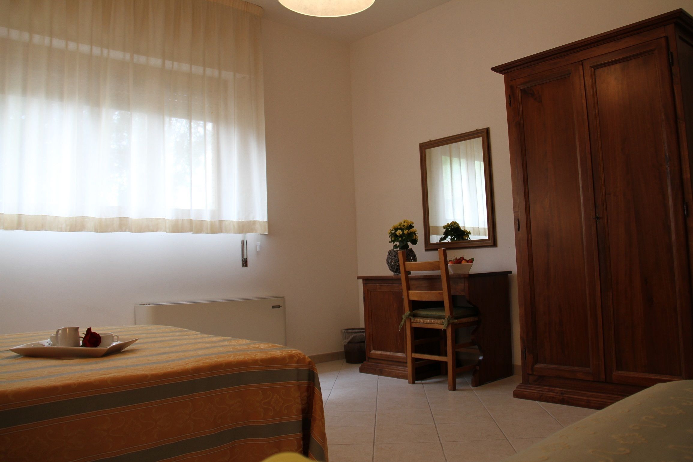 Ein Hotelzimmer mit einem Bett, einem Holzschrank, einem Schreibtisch mit Stuhl und einem Fenster mit leichtem Vorhang.