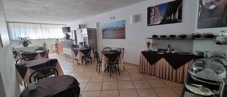 Un comedor con varias mesas y sillas, una barra con vitrina y obras de arte colgadas en la pared.