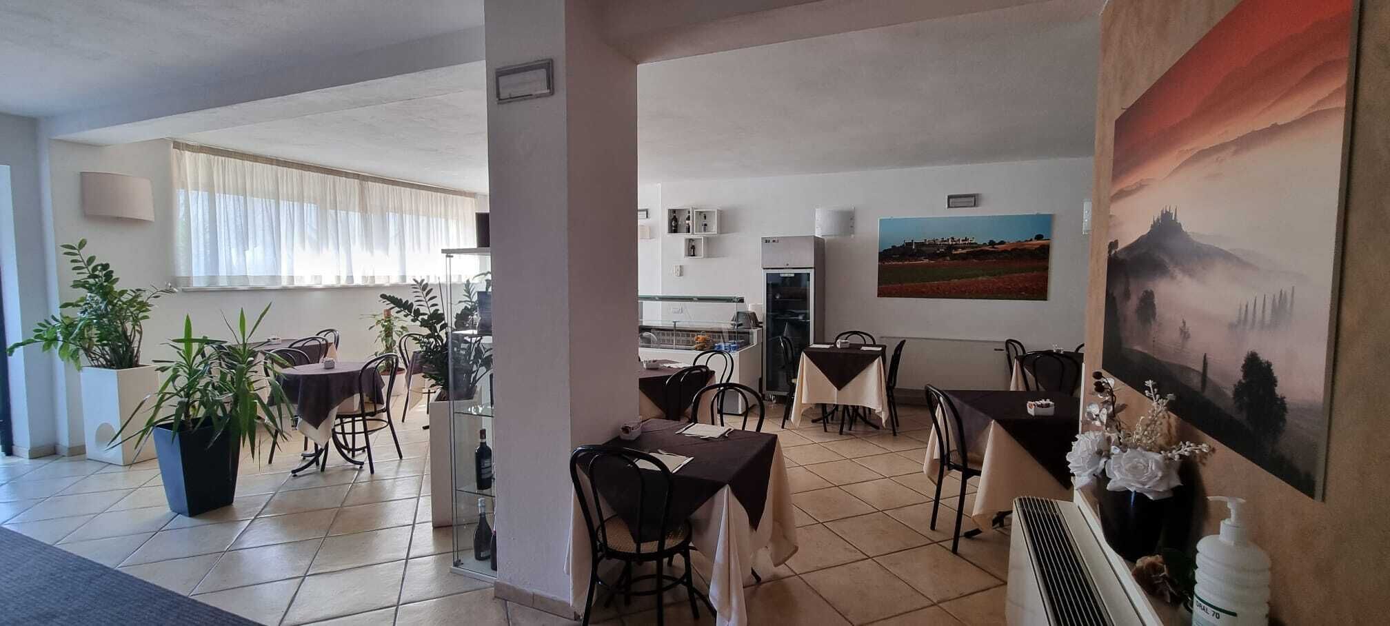 A dining area with tables and chairs, potted plants, and a painting on the wall.