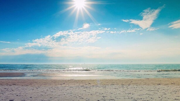 Een strand met een heldere lucht en een felle zon.