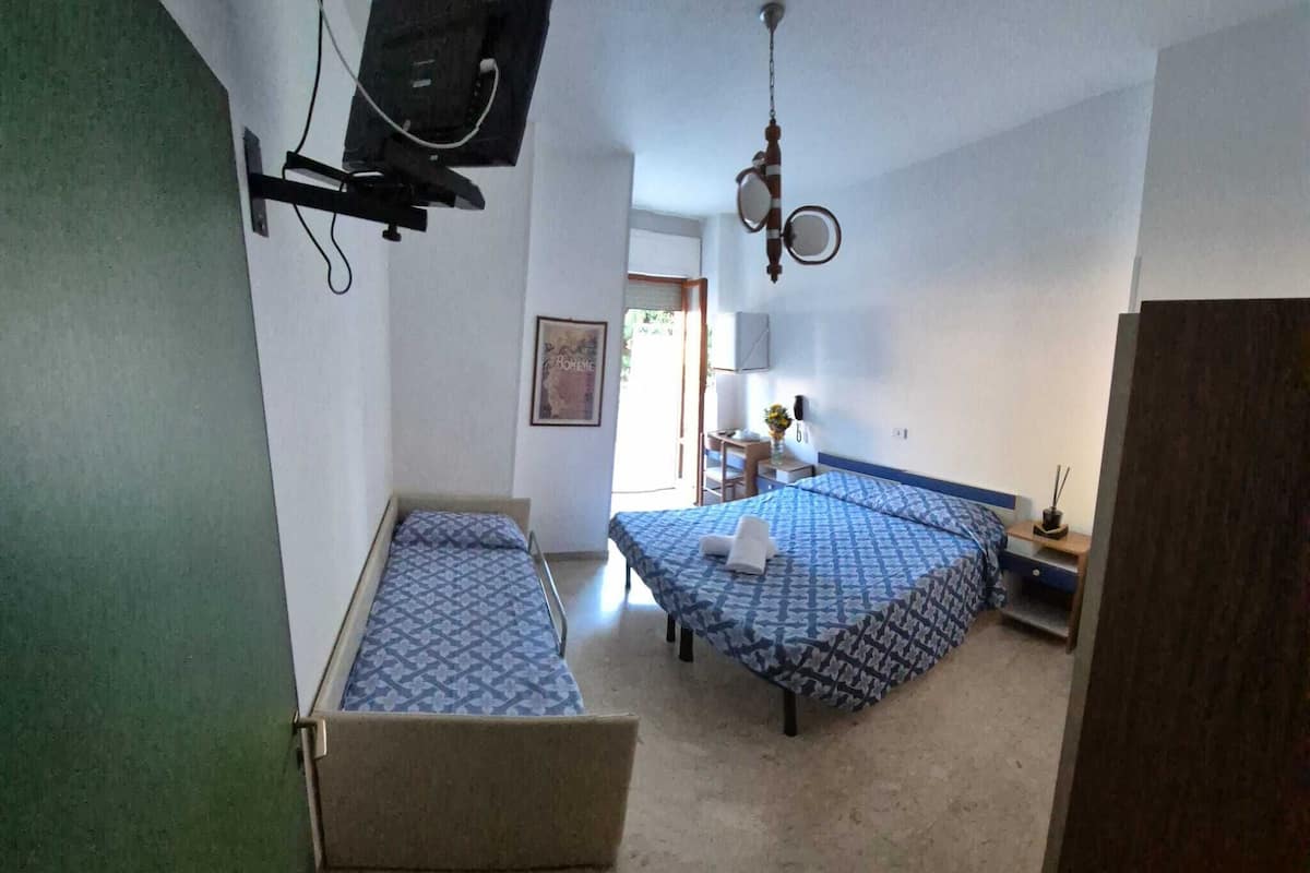 Una habitación con dos camas, un televisor montado en la pared, una mesita de noche con una lámpara y un cuadro enmarcado.