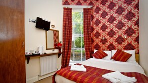 A hotel room with a bed, a television mounted on the wall, a window with curtains, and a radiator. - Leigh House Hotel (London)