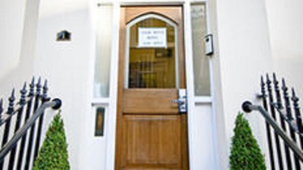 A hotel entrance with a wooden door, a red carpet, and two potted plants on either side. - Leigh House Hotel (London)