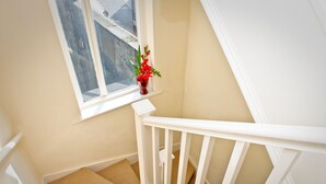 A staircase with a white railing, beige walls, and a window with a red flower vase. - Leigh House Hotel (London)