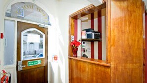 A wooden door with a sign above it, a fire extinguisher, and a red vase with flowers on a shelf. - Leigh House Hotel (London)