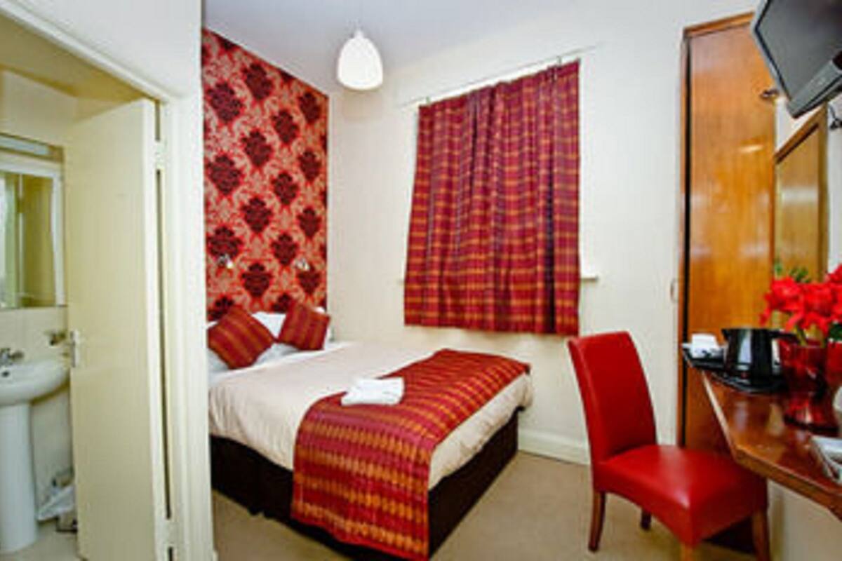 A bedroom with a bed, a red chair, a desk with a computer, and a window with red curtains.