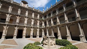 Un patio histórico con múltiples arcos y columnas, que presenta una fuente central y una estatua.
