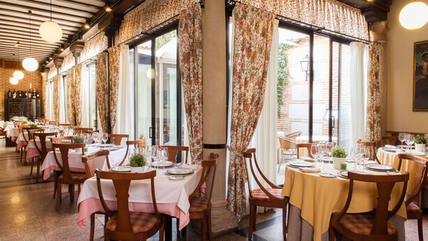 Un restaurante con varias mesas dispuestas para comer, con cortinas de flores y sillas de madera.