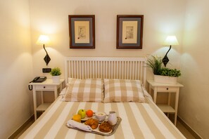 A neatly made bed with striped bedding, two bedside tables with lamps, framed pictures on the wall, and a tray with breakfast items. - Miguel de Cervantes (Alcala de Henares)