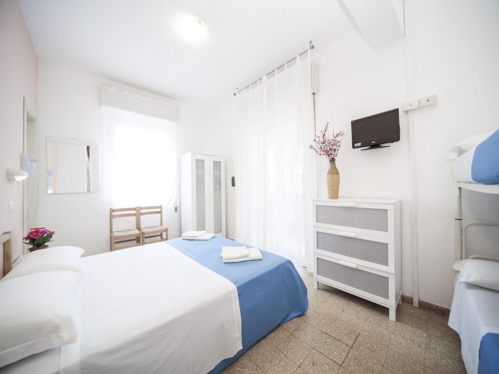 Una habitación de hotel con cama, una silla, armario, televisor y radiador.