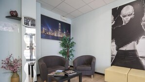 Una sala moderna con dos sillones, una mesa de centro, un cuadro grande de un paisaje urbano, una planta en maceta y un sofá amarillo.