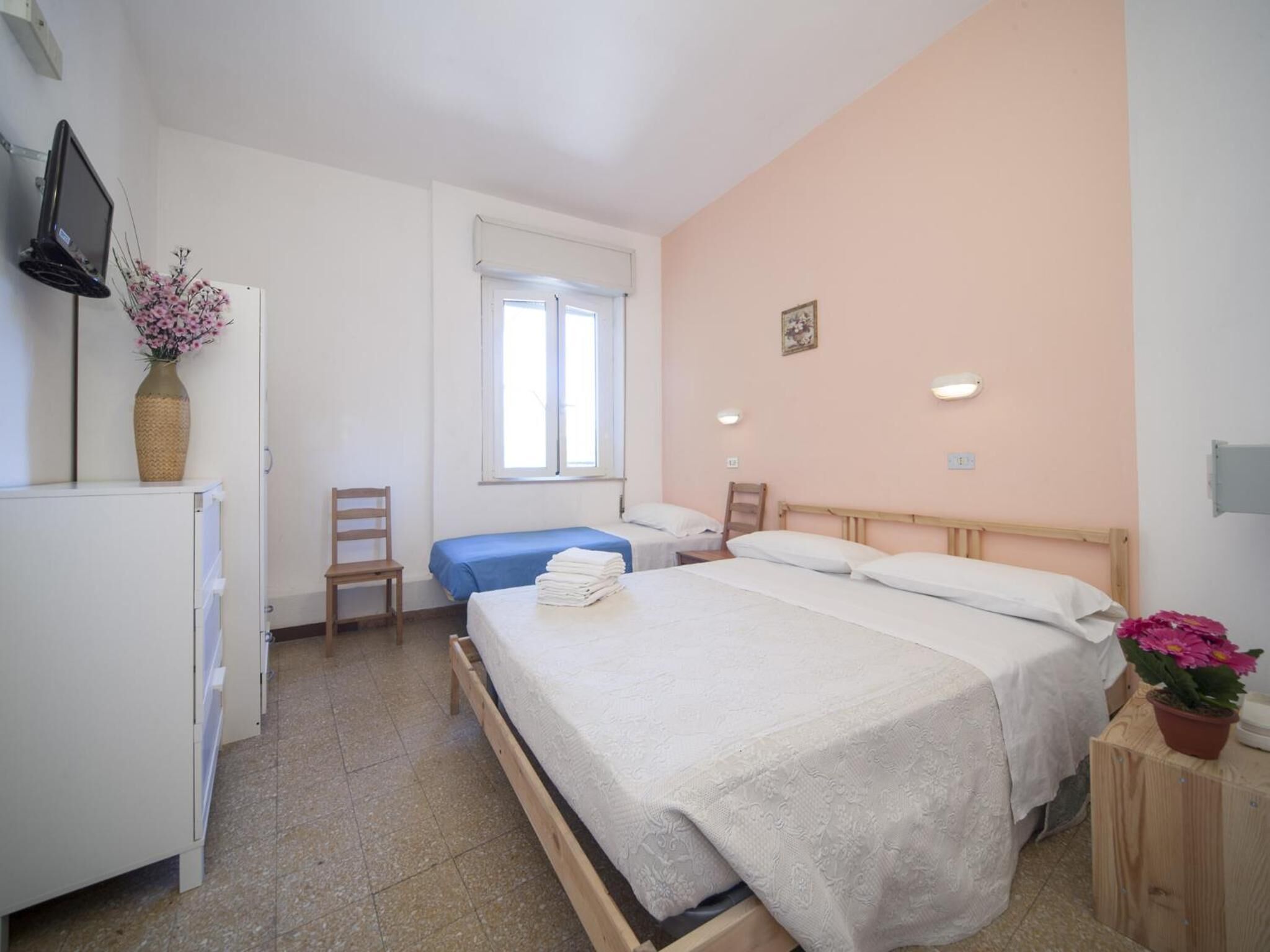 Ein Hotelzimmer mit einem großen Bett, einem kleineren Bett, einem Schreibtisch, einem Stuhl, einem Fernseher und einem Fenster.