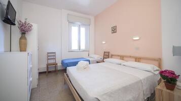 Ein Hotelzimmer mit einem großen Bett, einem kleineren Bett, einem Schreibtisch, einem Stuhl, einem Fernseher und einem Fenster.