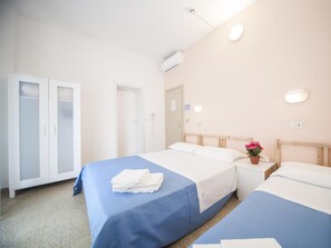 A hotel room with two beds, a wardrobe, a bedside table with a lamp, and a potted plant. - Hotel Colombo (Riccione)