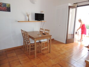 A dining area with a wooden table and chairs, a television on a shelf, and a sliding glass door leading to an outdoor area.