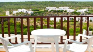 A terrace with a round table and four chairs, overlooking a green landscape with buildings in the distance. - Apartamentos Sa Cala (Ciutadella de Menorca)