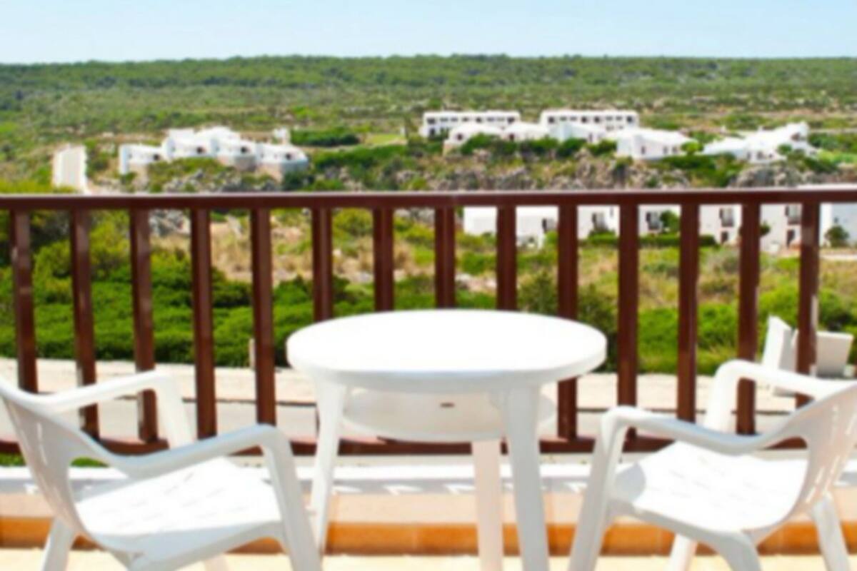 Una terraza con una mesa redonda y cuatro sillas, con vistas a un paisaje verde y edificios a lo lejos.