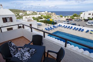 Zona junto a la piscina con sillones de descanso, una mesa y vista al mar y edificios al fondo.