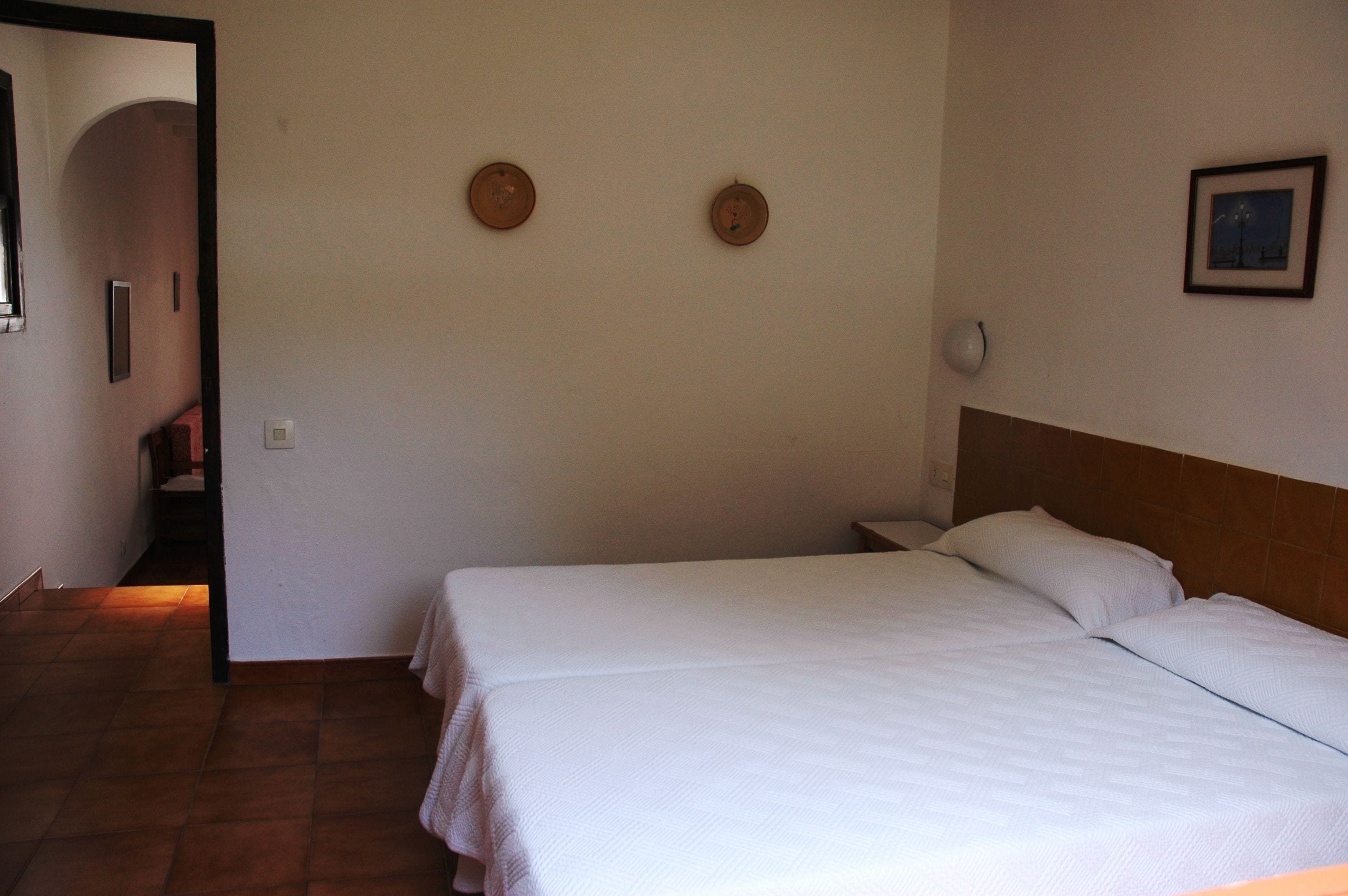 A bedroom with two beds, a wooden headboard, a nightstand, a wall clock, and a framed picture.