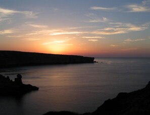 Un atardecer costero con aguas tranquilas y acantilados rocosos.